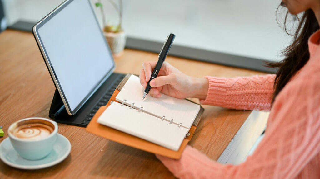 women writing a checklist in front of a tablet with a cup of coffee